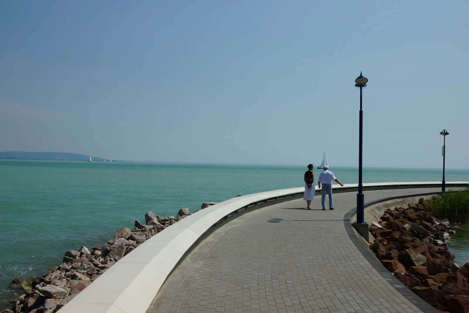 The renovated pier of the Tihany public ferry port with a curved white cast-stone parapet wall and small-element paving, Lake Balaton in the background
