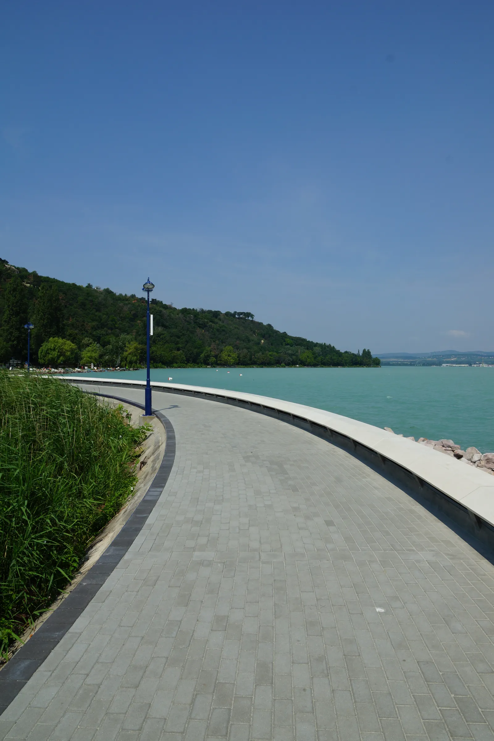 The lakeside promenade leading to the port, with reeds and the green Tihany hillside, and turquoise Balaton water