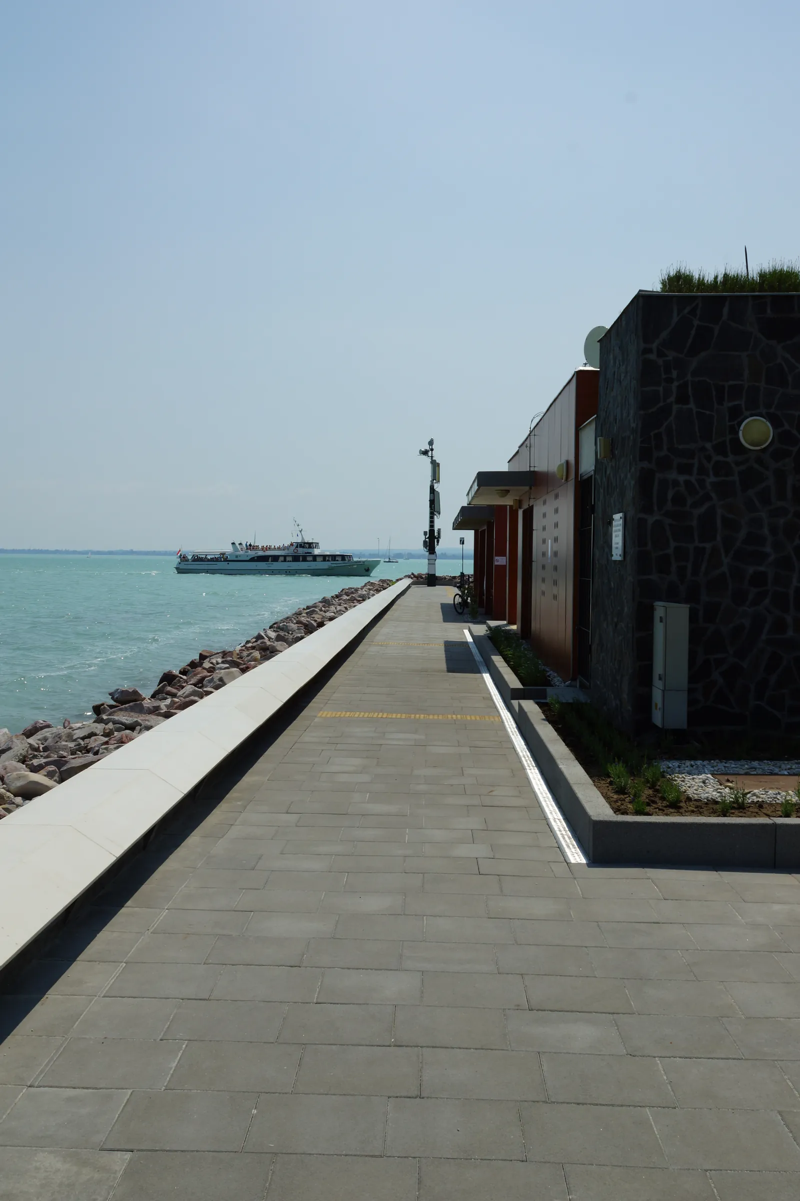 The port's natural-stone-clad building with a green roof, the promenade alongside, and a passenger ferry on the water